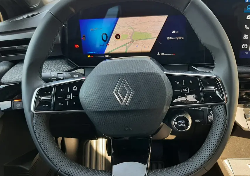 Vue frontale du volant noir perforé de la Renault Clio VI TCe 115ch Techno avec tableau de bord numérique affichant une carte.