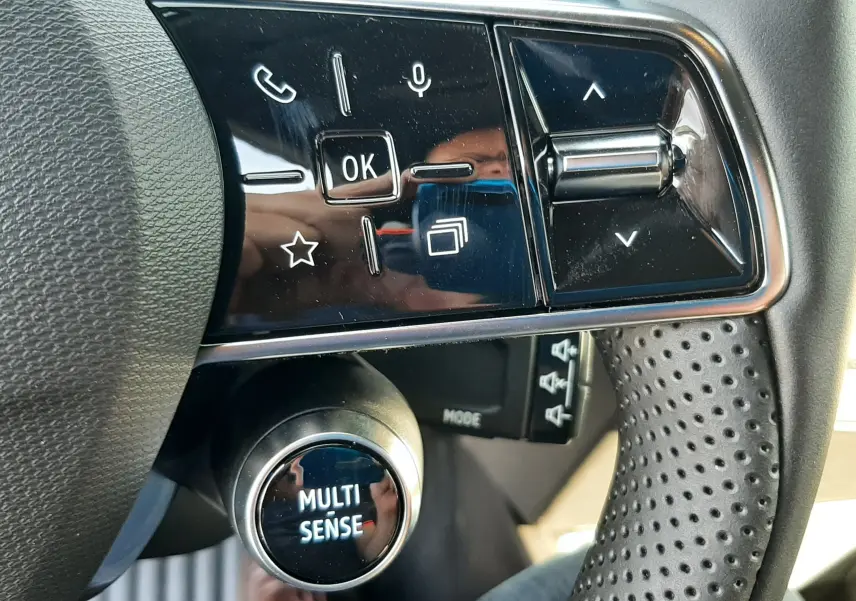 Gros plan sur les commandes multifonctions noires et brillantes du volant perforé côté gauche de la Renault Clio VI Gris Rafale.