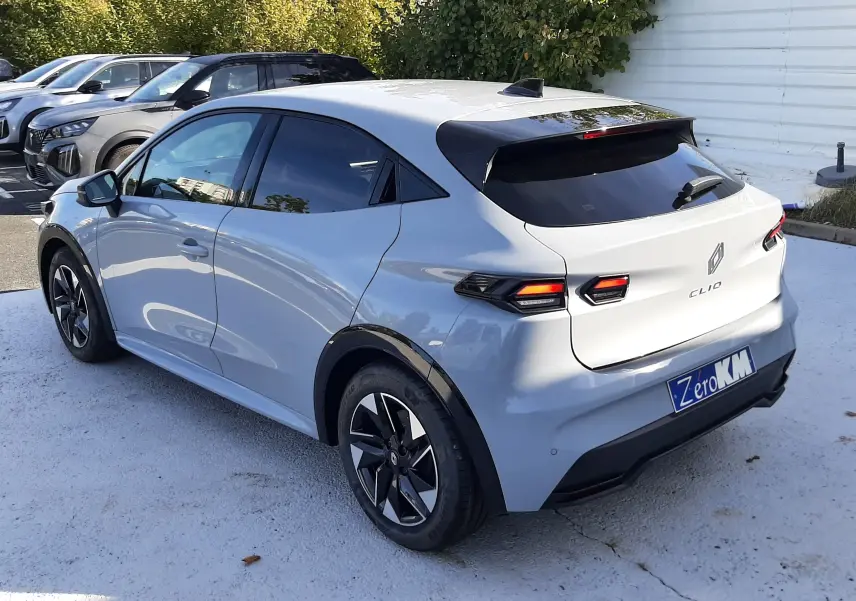 Vue 3/4 arrière droite d'une Renault Clio VI gris Rafale avec feux arrière LED et jantes noires, stationnée en extérieur.