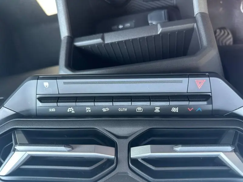 Vue rapprochée du tableau de bord du Dacia Duster blanc, montrant les commandes de climatisation et les aérateurs centraux.