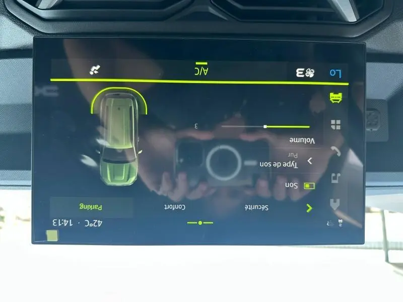 Écran tactile central du Dacia Duster blanc 2025 montrant l'interface de réglage sonore et climatisation.