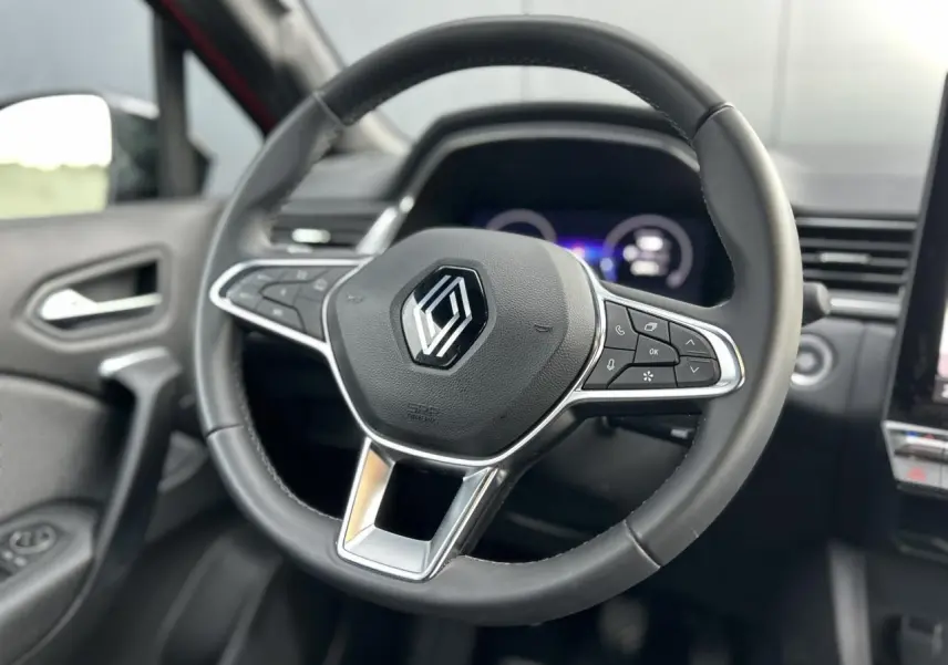 Vue rapprochée du volant noir du Renault Captur 2025, avec commandes intégrées et tableau de bord numérique flou en arrière-plan.