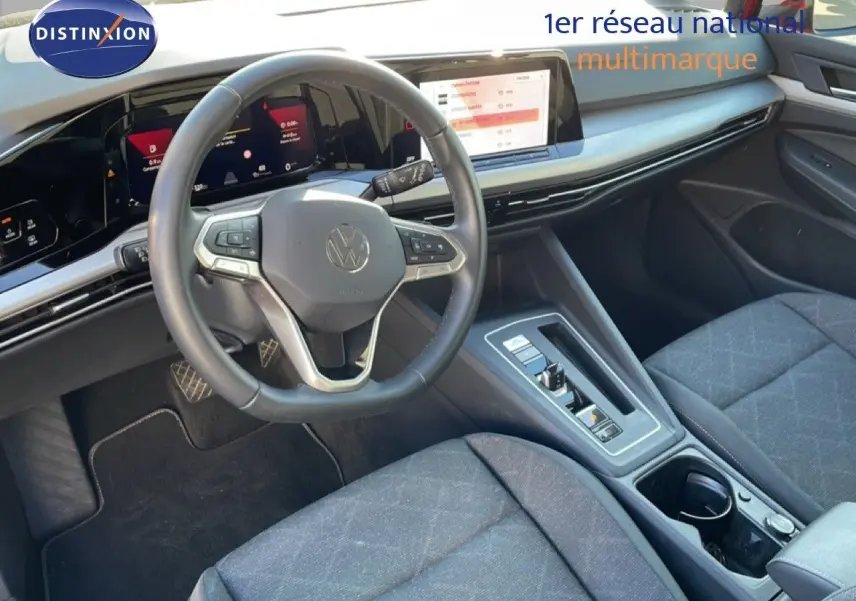 Vue intérieure de la Volkswagen Golf VIII 2023, tableau de bord et volant multifonction en cuir, sièges tissu gris.