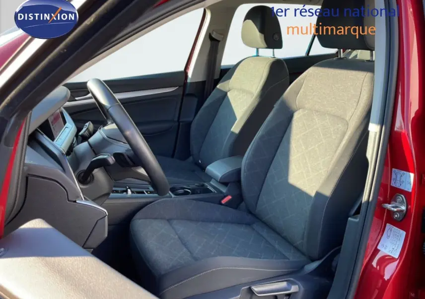 Vue intérieure côté conducteur de la Volkswagen Golf VIII rouge, sièges tissu gris et volant multifonction noir.