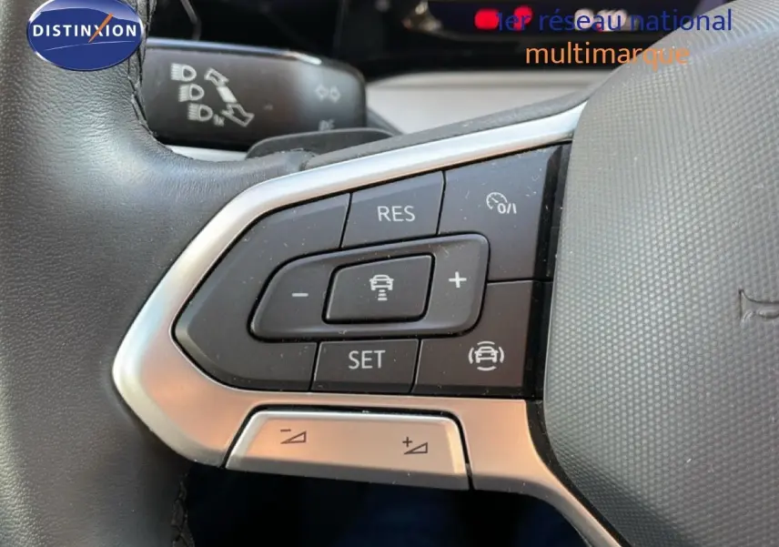 Gros plan sur les commandes au volant côté gauche de la Volkswagen Golf VIII rouge, mettant en valeur les boutons de régulateur de vitesse.