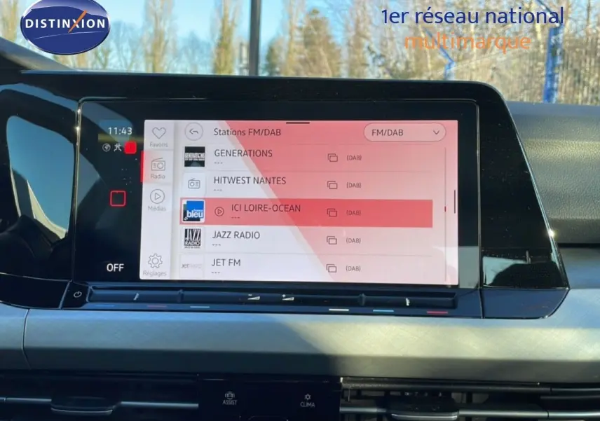 Écran tactile central de la Volkswagen Golf VIII rouge Roi Metal, affichant les stations radio FM/DAB en intérieur.