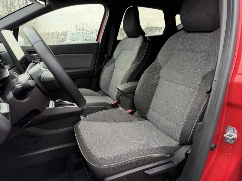 Vue intérieure côté conducteur du Renault Captur 2025 Rouge Flamme, mettant en valeur les sièges en tissu gris et la porte ouverte.