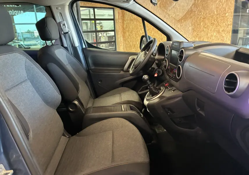 Vue intérieure côté conducteur du Citroën Berlingo Multispace bleu, montrant les sièges en tissu gris et la console centrale avec boîte manuelle.