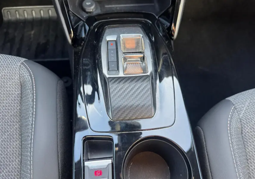 Vue rapprochée de la console centrale noire du Peugeot 2008 Hybrid 136 e-DCS6 Allure avec sélecteur de vitesse et frein à main électrique.