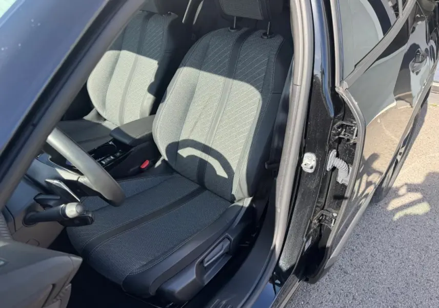 Vue intérieure côté conducteur du Peugeot 2008 Hybrid noir 2025, mettant en valeur le siège avant en tissu et l'ouverture de porte.