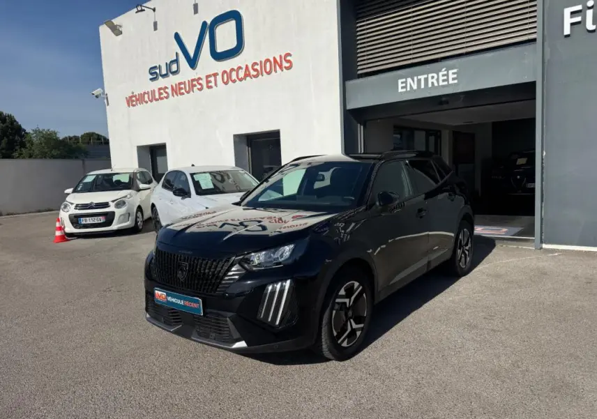 Peugeot 2008 Hybrid noir en 3/4 avant droit, avec barres de toit et jantes alliage 17 pouces, devant un garage.