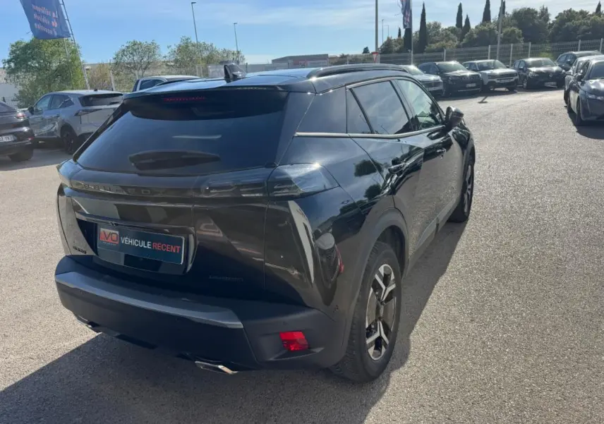 Vue 3/4 arrière droite d’un Peugeot 2008 Hybrid noir avec jantes alliage 17 pouces et barres de toit visibles.