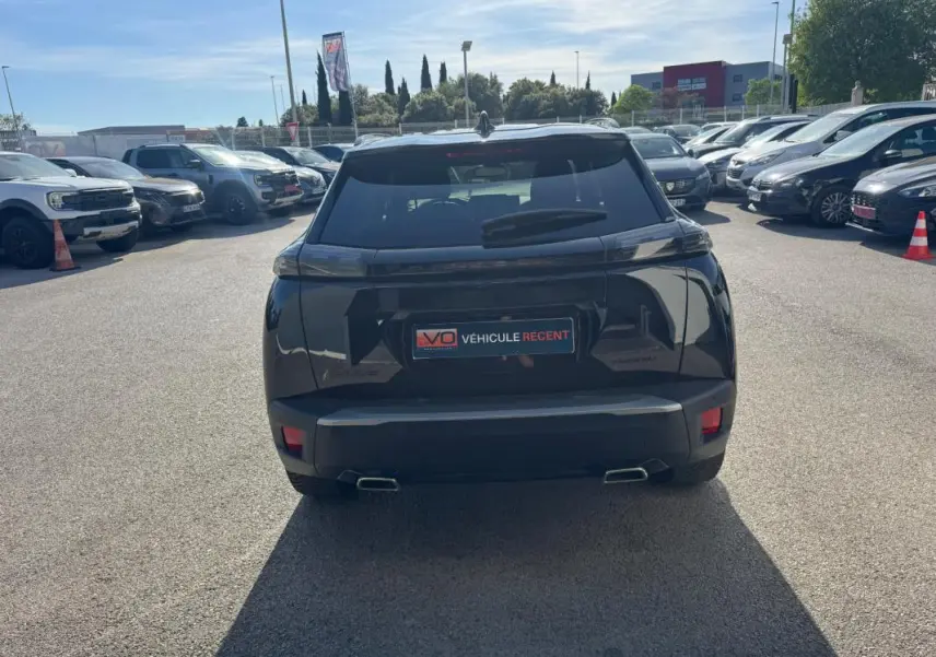 Vue arrière d’un Peugeot 2008 Hybrid 136 noir avec barres de toit et jantes alliage 17 pouces, stationné en extérieur.