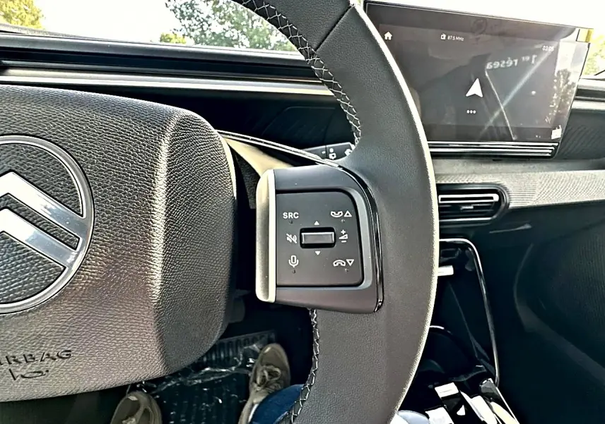 Vue rapprochée du volant noir de la Citroën C3 Aircross 2026, avec commandes audio et écran tactile en arrière-plan.