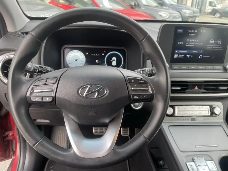 Vue intérieure centrée sur le volant d'un Hyundai Kona électrique rouge métal 2021, avec tableau de bord numérique et écran tactile.