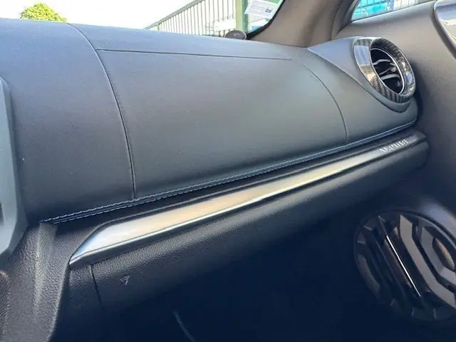 Gros plan sur la console centrale carbone de l'Alpine A110 gris acier avec bouton start/stop rouge et cuir noir surpiqué bleu.