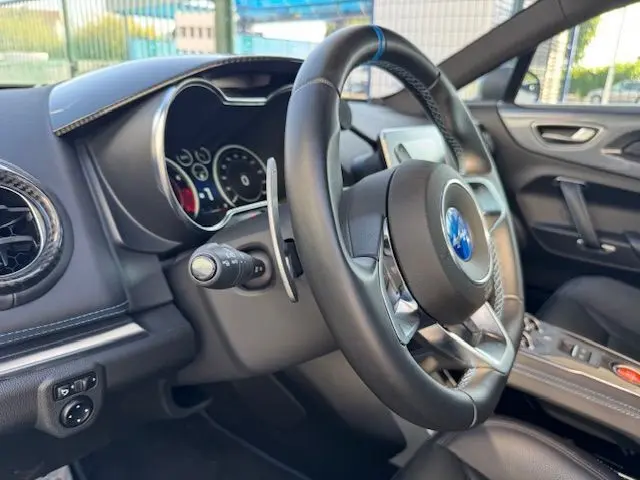 Intérieur de l'Alpine A110 1.8T 252 Légende 2021, vue côté gauche sur volant cuir avec surpiqûres bleues et tableau de bord numérique.