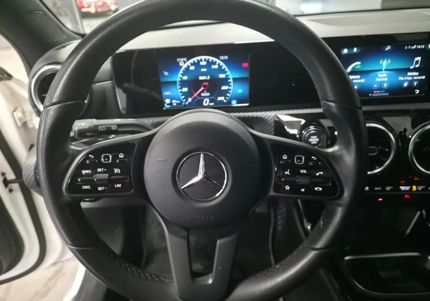 Vue rapprochée du volant cuir noir de la Mercedes Classe A 160 Style Line 2019 avec tableau de bord digital et écran tactile.