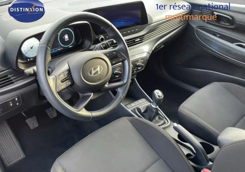 Vue intérieure côté conducteur de la Hyundai i20 2025 avec volant, tableau de bord numérique et levier de vitesses manuel.