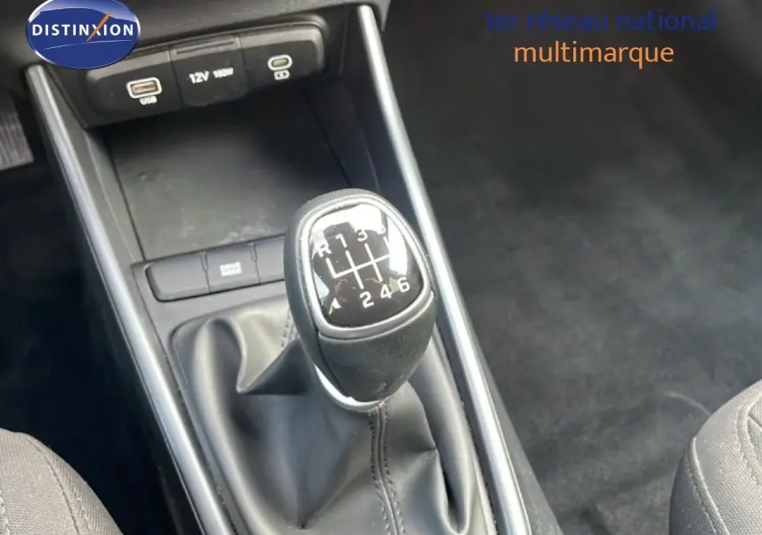 Gros plan sur le levier de vitesses manuel noir de la Hyundai i20 2025, avec console centrale et prises USB visibles.