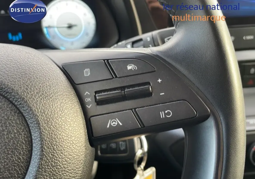 Gros plan sur le volant côté droit d'une Hyundai i20 2025, avec commandes de régulateur et tableau de bord flou en arrière-plan.