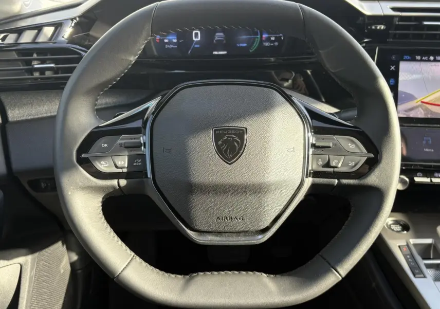 Vue rapprochée du volant cuir noir de la Peugeot 308 Hybrid 2025 avec tableau de bord numérique et écran tactile.
