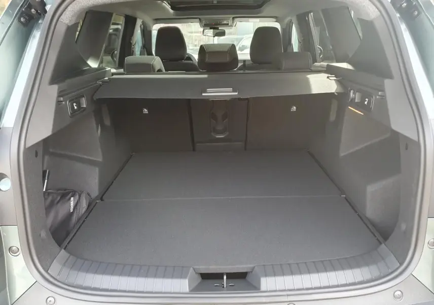 Coffre ouvert vu de l'arrière du Dacia Bigster vert cèdre, avec banquette arrière rabattue et cache-bagages en place.