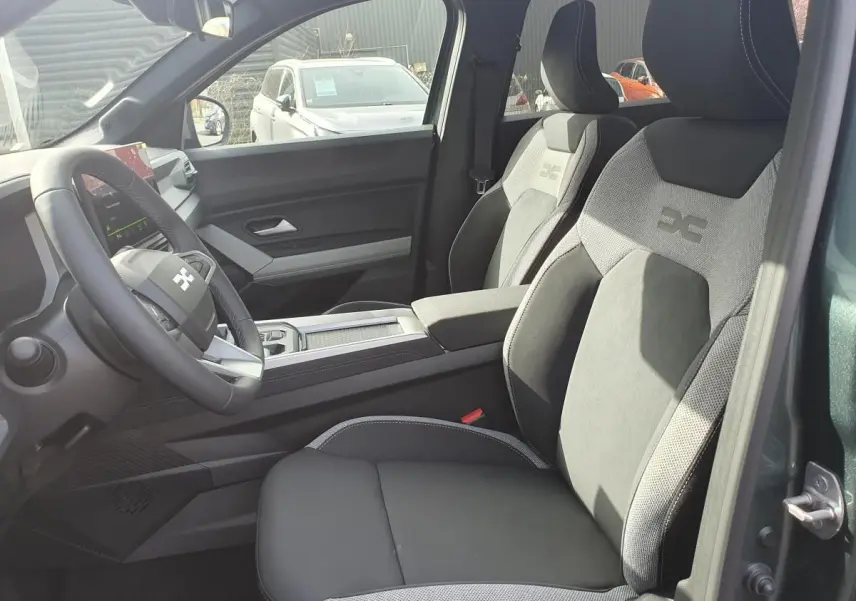 Vue intérieure côté conducteur du Dacia Bigster 2026 vert cèdre, sièges tissu gris avec logo brodé sur appuie-tête.