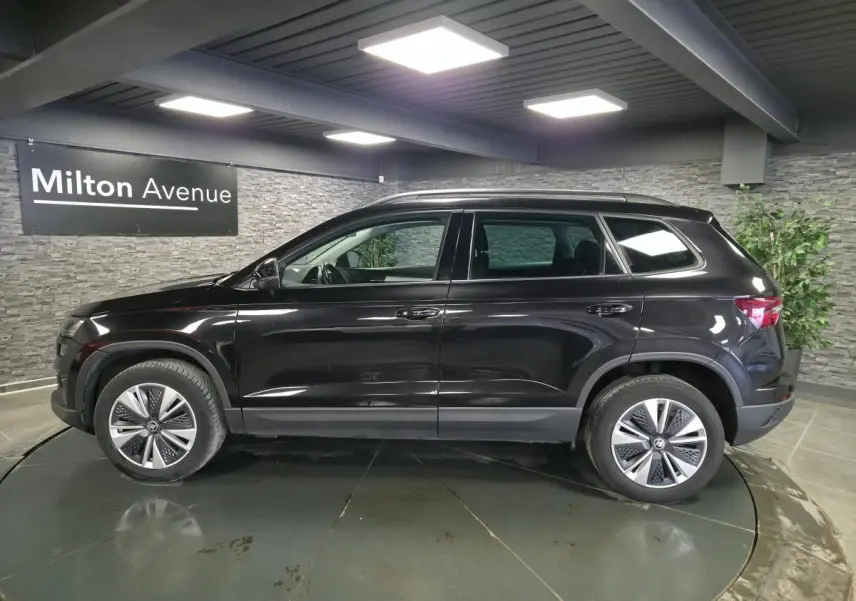 Vue de profil côté gauche d’un Skoda Karoq noir 2023 en intérieur, avec jantes alliage et vitres surteintées.