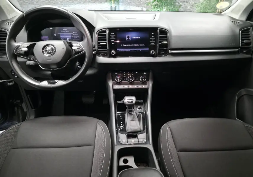 Vue intérieure frontale du tableau de bord et console centrale noire du Skoda Karoq 2023 avec volant cuir et écran tactile.