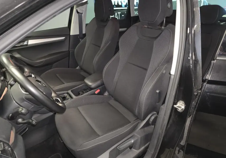 Vue intérieure côté conducteur du Skoda Karoq noir 2023, sièges tissu Ambition noirs avec accoudoir central.