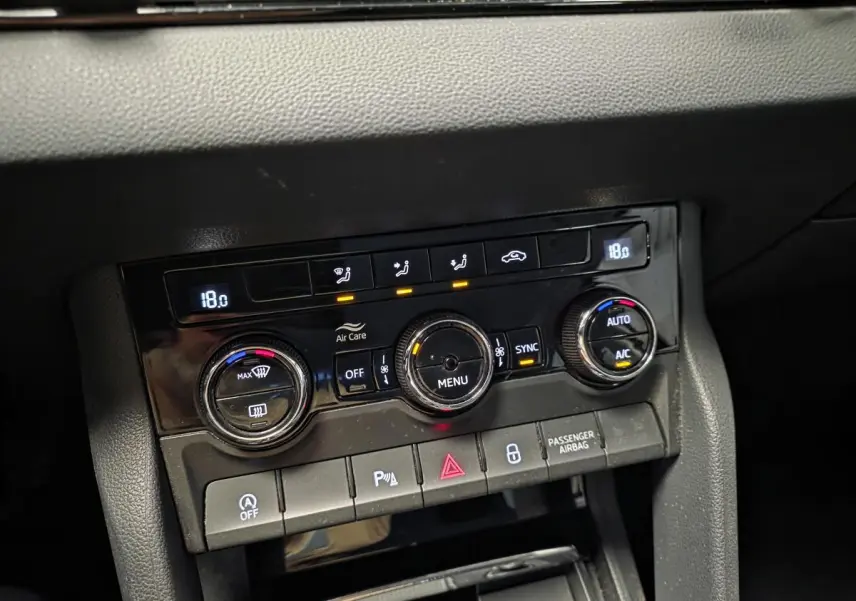 Gros plan sur la console centrale noire du Skoda Karoq 2023, avec commandes de climatisation automatique bi-zone et boutons fonctionnels.