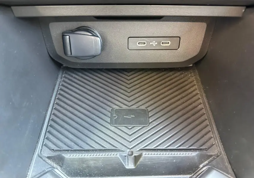Gros plan sur la console centrale du Dacia Duster 2025 avec prise 12V, deux ports USB-C et surface de charge sans fil noire.