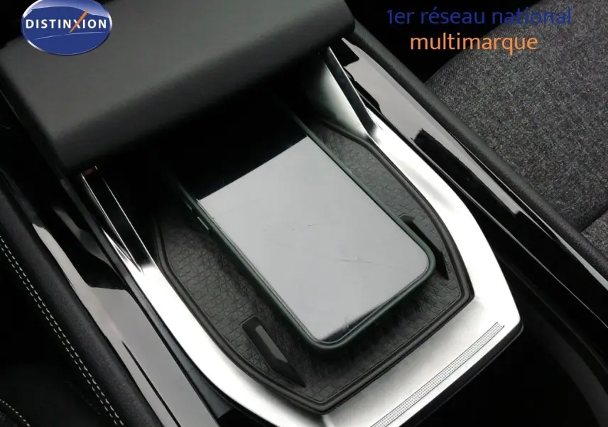 Gros plan sur la console centrale noire du Renault Austral E-Tech avec un smartphone posé sur le chargeur sans fil.