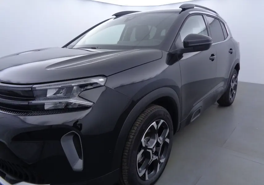 Vue 3/4 avant droit d'un Citroën C5 Aircross noir métal avec jantes bi-ton et barres de toit visibles.
