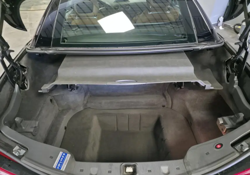 Coffre ouvert vu de l'arrière d'une Mercedes SL 500 noire, avec intérieur de coffre en tissu gris.