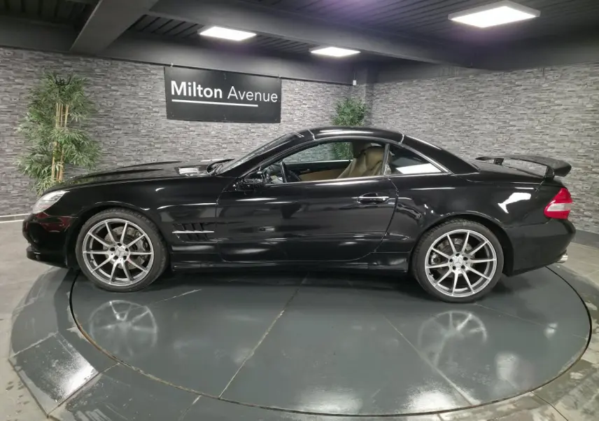 Profil côté gauche d'une Mercedes SL 500 noire avec jantes alliage 19 pouces et aileron arrière en intérieur showroom.