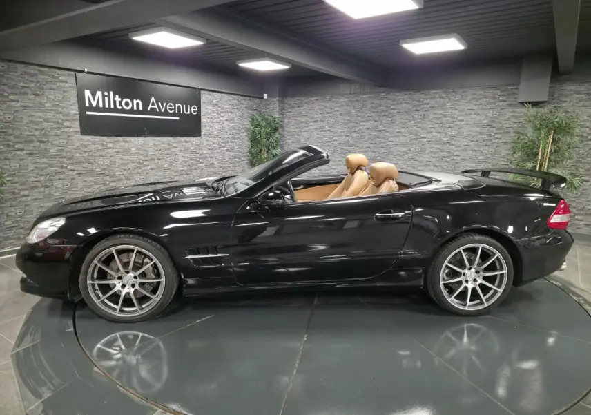 Vue de profil côté gauche d'une Mercedes SL 500 noire cabriolet avec intérieur cuir beige et jantes alliage 19 pouces.