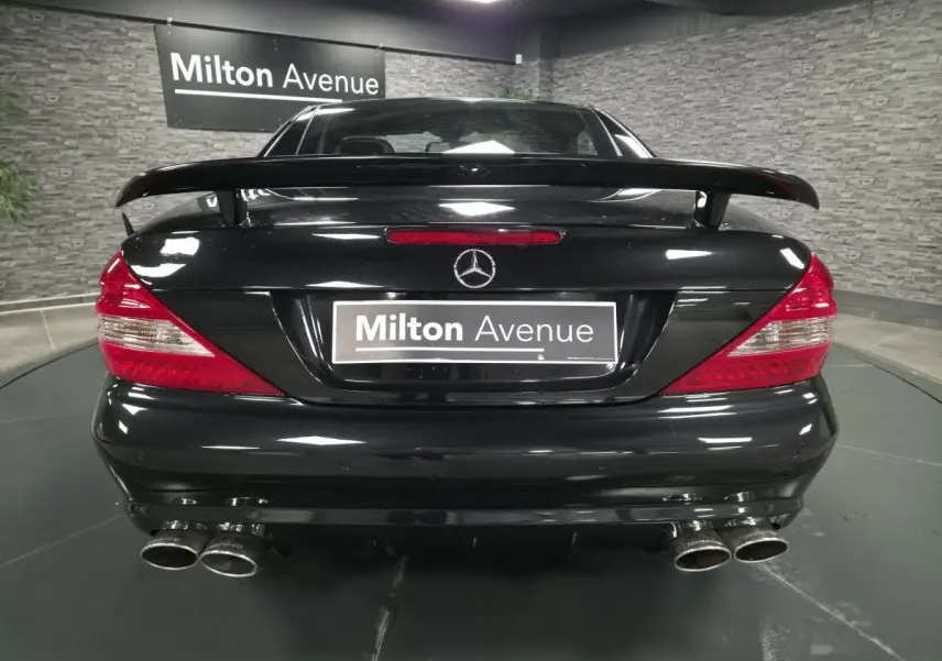 Vue arrière d'une Mercedes SL 500 noire avec aileron et quadruple sortie d'échappement dans un showroom.
