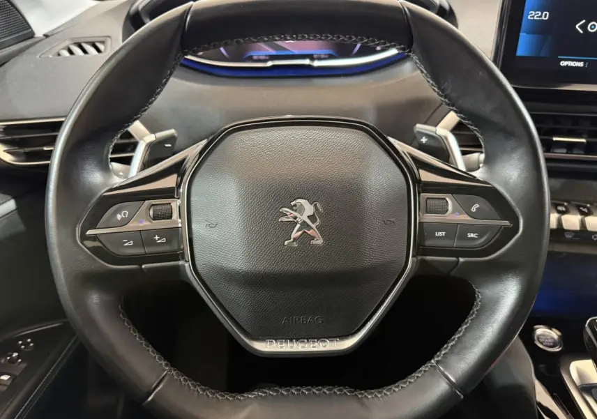 Gros plan sur le volant cuir noir du Peugeot 5008 2021 avec commandes intégrées et tableau de bord numérique bleu.