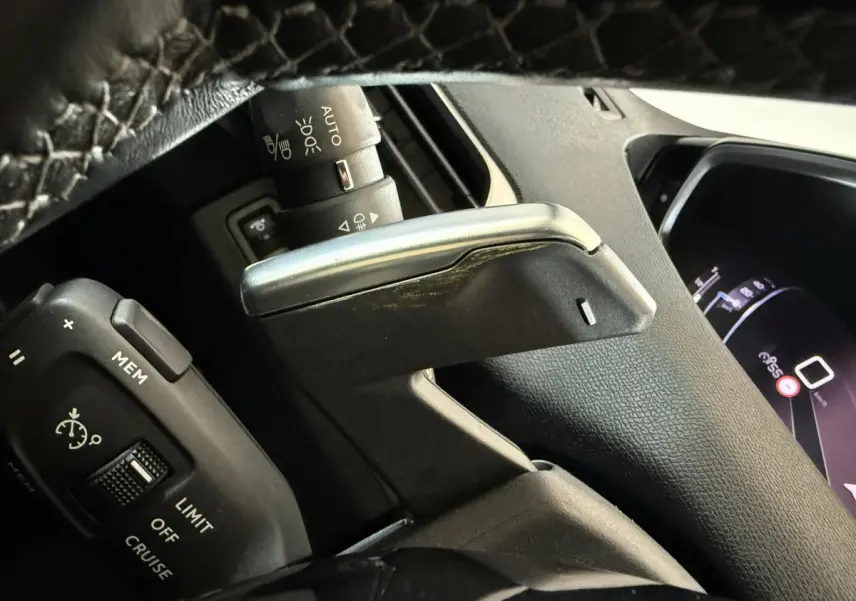 Gros plan sur le levier de commande et le volant en cuir noir du Peugeot 5008 gris clair, tableau de bord numérique partiellement visible.