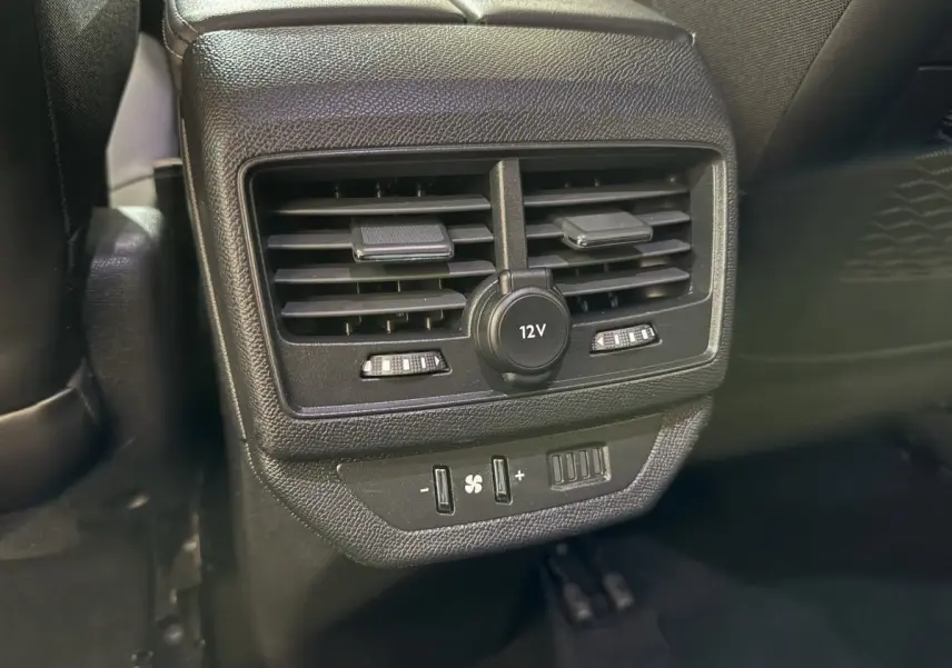 Détail de la console arrière noire avec prise 12V et commandes de ventilation du Peugeot 5008 gris clair, vue intérieure rapprochée.