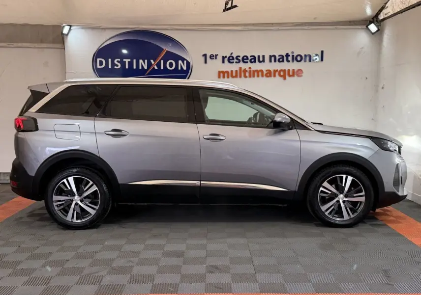 Vue latérale droite d’un Peugeot 5008 gris clair 2021 avec jantes alliage et vitres teintées en intérieur showroom.