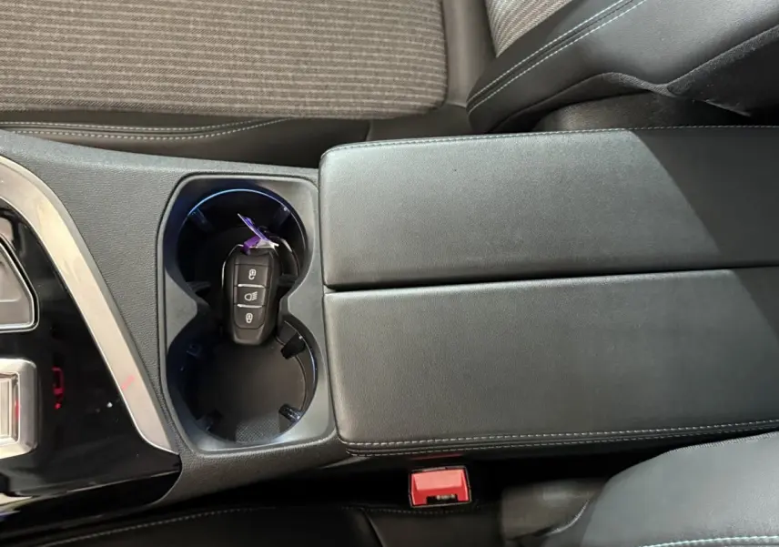Vue rapprochée de la console centrale noire avec porte-gobelets et clé de voiture dans un Peugeot 5008 gris clair.