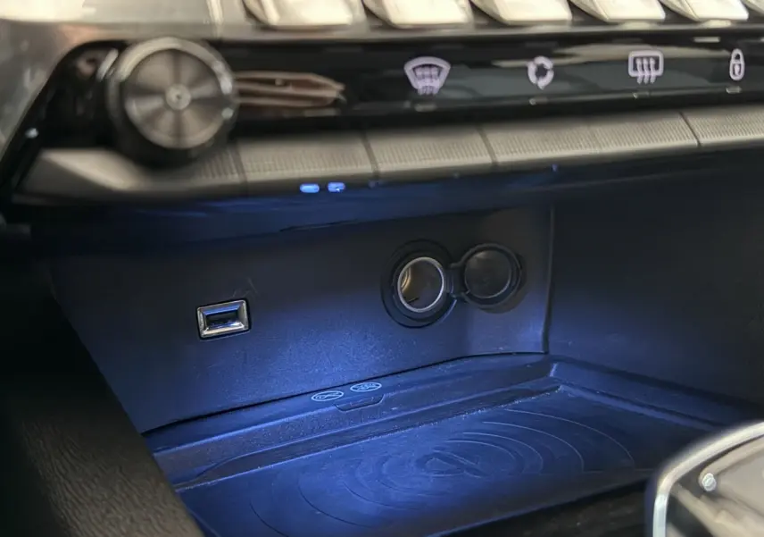 Gros plan sur la console centrale du Peugeot 5008 2021, montrant prise USB, prise 12V et surface de charge sans fil éclairée.