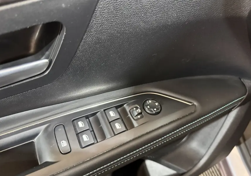 Gros plan sur la commande des vitres électriques côté conducteur du Peugeot 5008 gris clair, avec surpiqûres bleues.