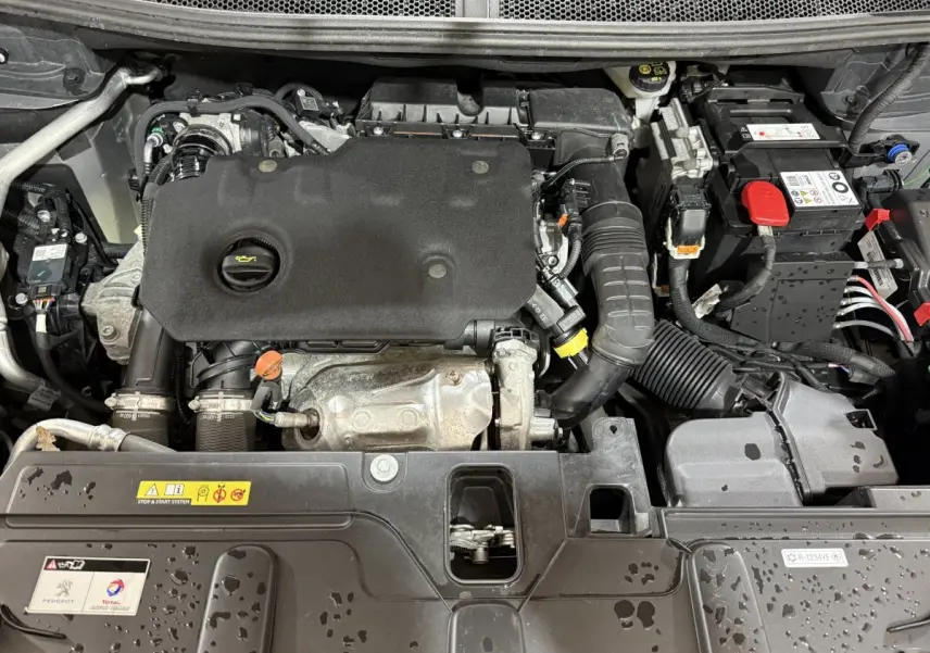 Vue rapprochée du moteur diesel Peugeot 5008 2021, avec capot ouvert et composants visibles sous la pluie.