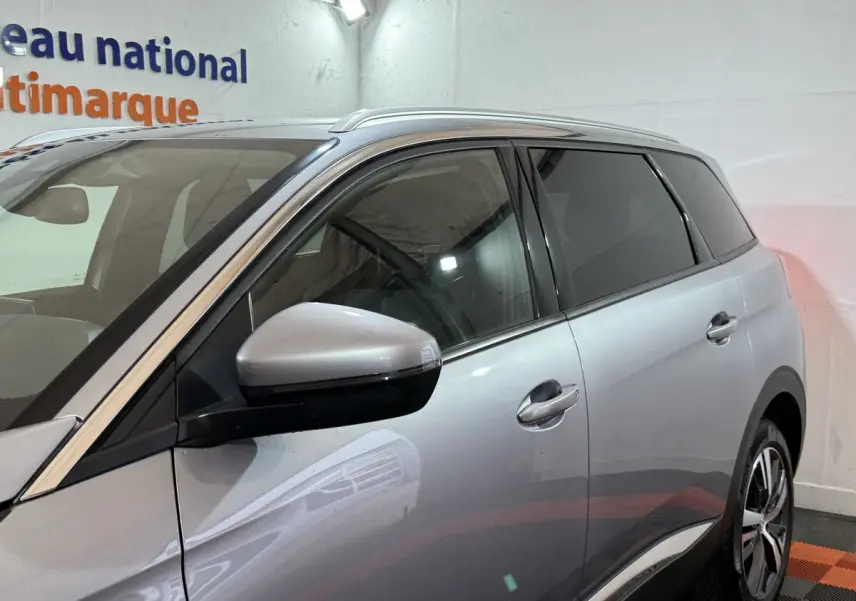 Vue côté gauche d'un Peugeot 5008 gris clair, mettant en valeur les vitres teintées et les rétroviseurs intégrant des clignotants.