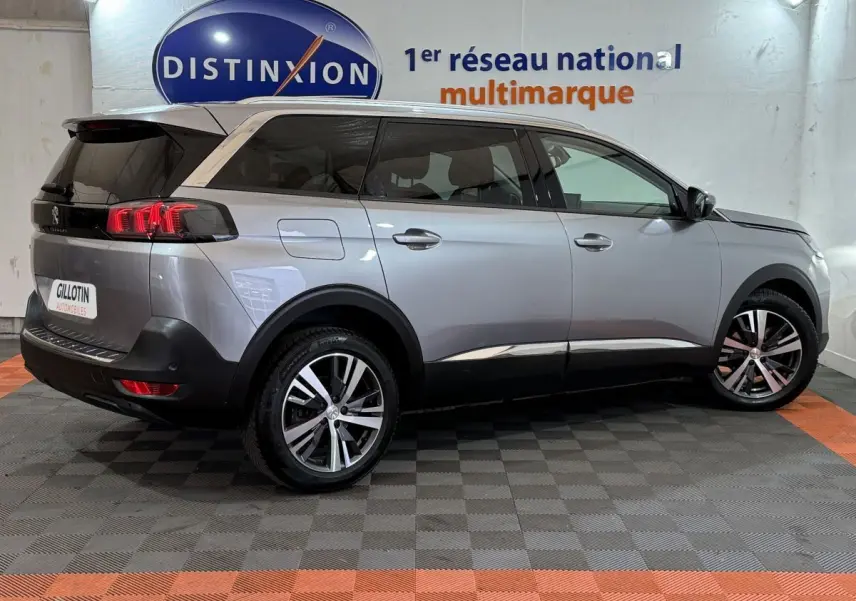 Peugeot 5008 gris clair vue de profil droit, avec vitres teintées et jantes alliage bicolores en intérieur showroom.