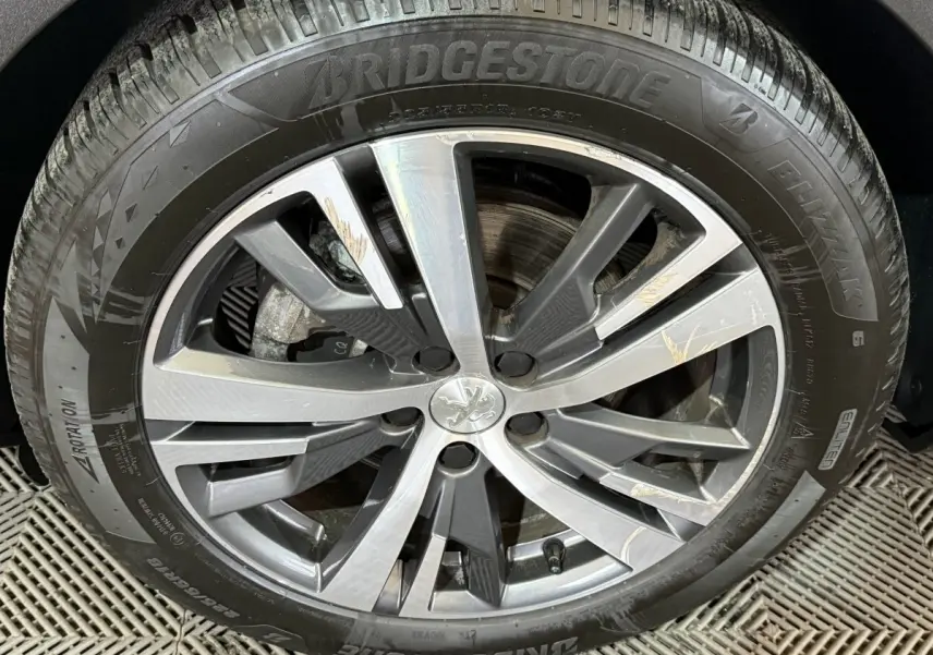 Gros plan sur la jante alliage gris et argentée avec logo Peugeot, montée sur pneu Bridgestone Blizzak.